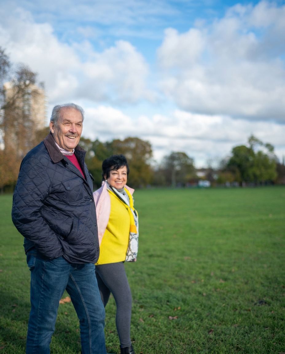 An older couple smiling as they walk together outdoors in a park.